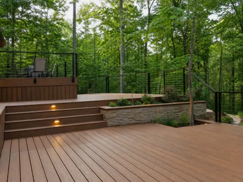 Two-level deck with lit steps at the edge of a wooded yard