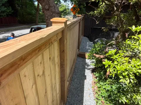 New wood privacy fence with post caps beside a gravel path