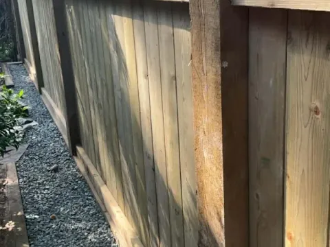Wood privacy fence with framed panels and capped posts along a gravel side yard