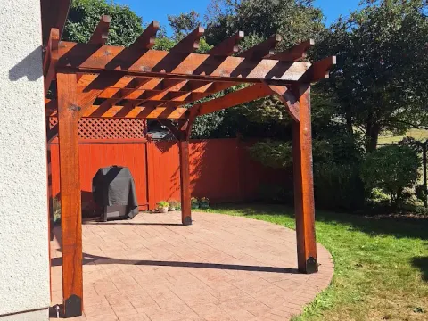 Stained wood pergola over a round stamped-concrete patio beside a house